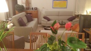 A living room with two sofas, a coffee table, and a television. There are plants and a lamp in the room. - Luxurious 3 bedroom villa with private pool garden and sea view (Kouklia)