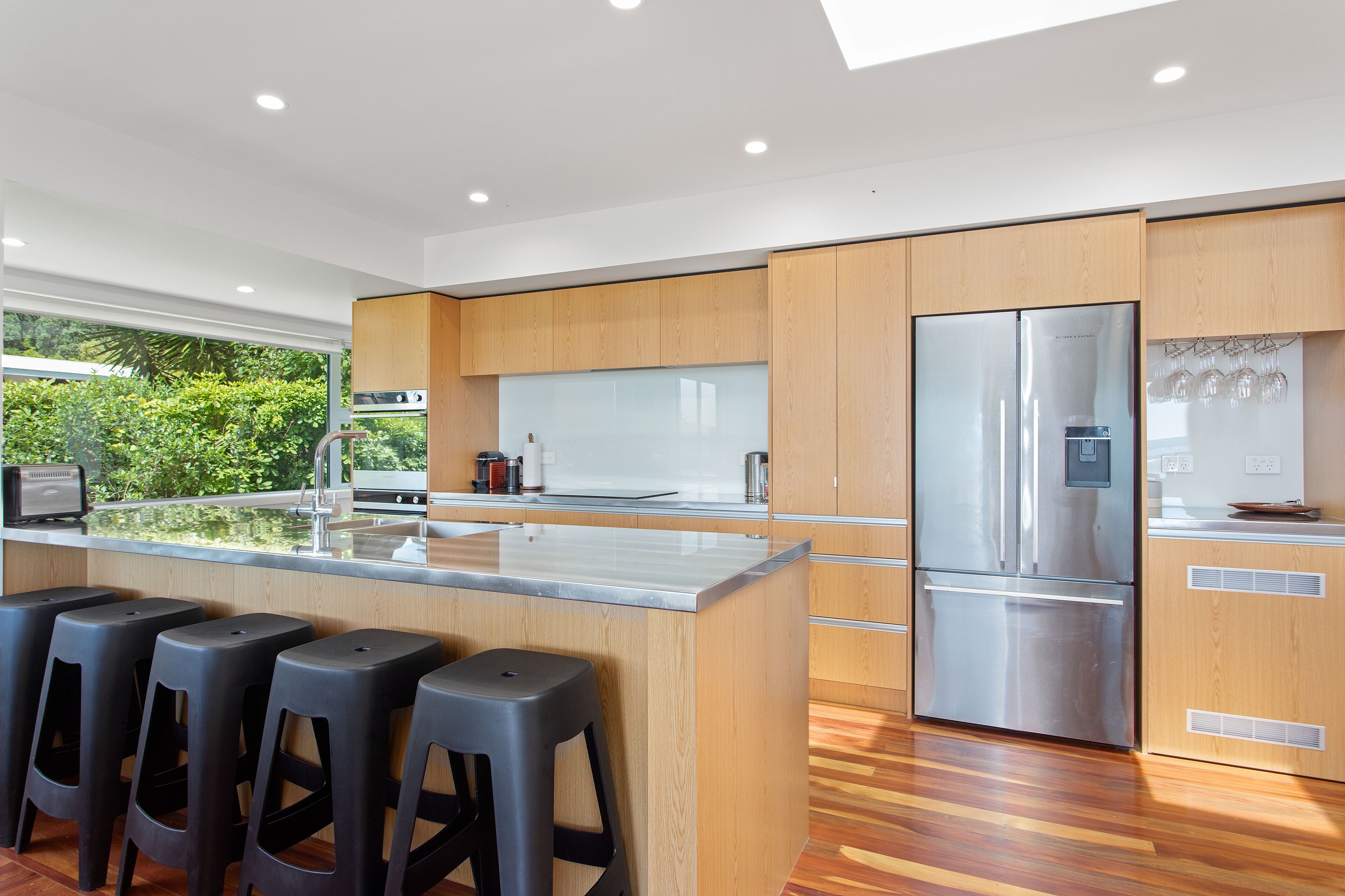 A modern kitchen with wooden cabinets, a stainless steel refrigerator, and a bar area with stools.