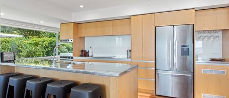 A modern kitchen with wooden cabinets, a stainless steel refrigerator, and a bar area with stools.