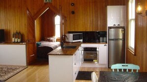 A compact kitchen with a microwave, oven, and refrigerator. An exit sign is visible above the doorway. - Revamped church in an old gold mining village (Central Otago District)