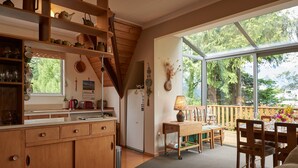 A kitchen with wooden cabinets, a dining area with a table and chairs, and a large window with a view of trees. - Retro Retreat - Queenstown Holiday Home (Queenstown)