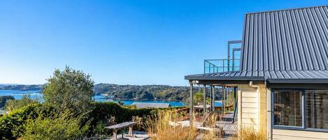 A modern house with a deck overlooking a body of water, surrounded by greenery.
