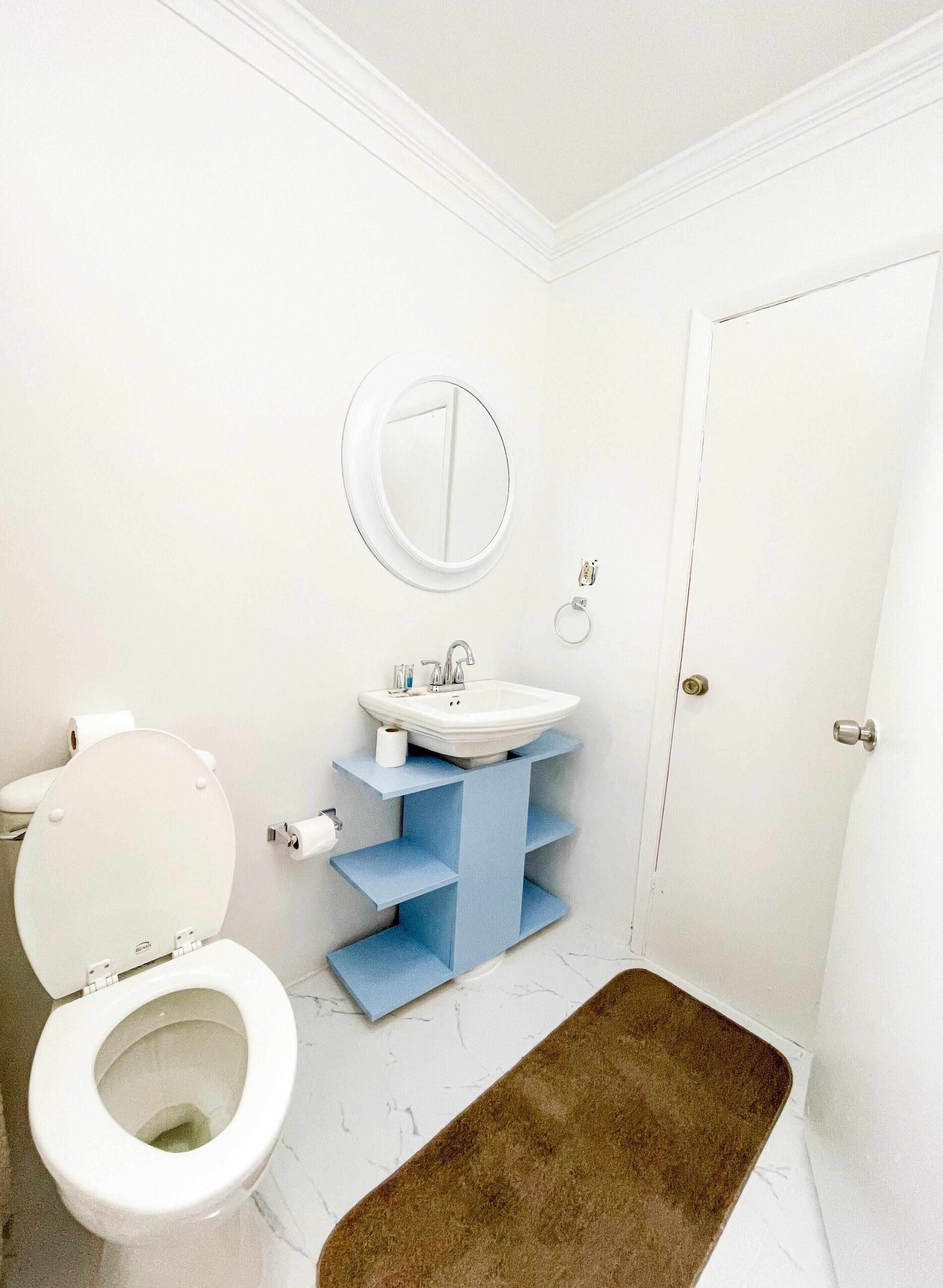 Un baño con inodoro, lavamanos, espejo y puerta.