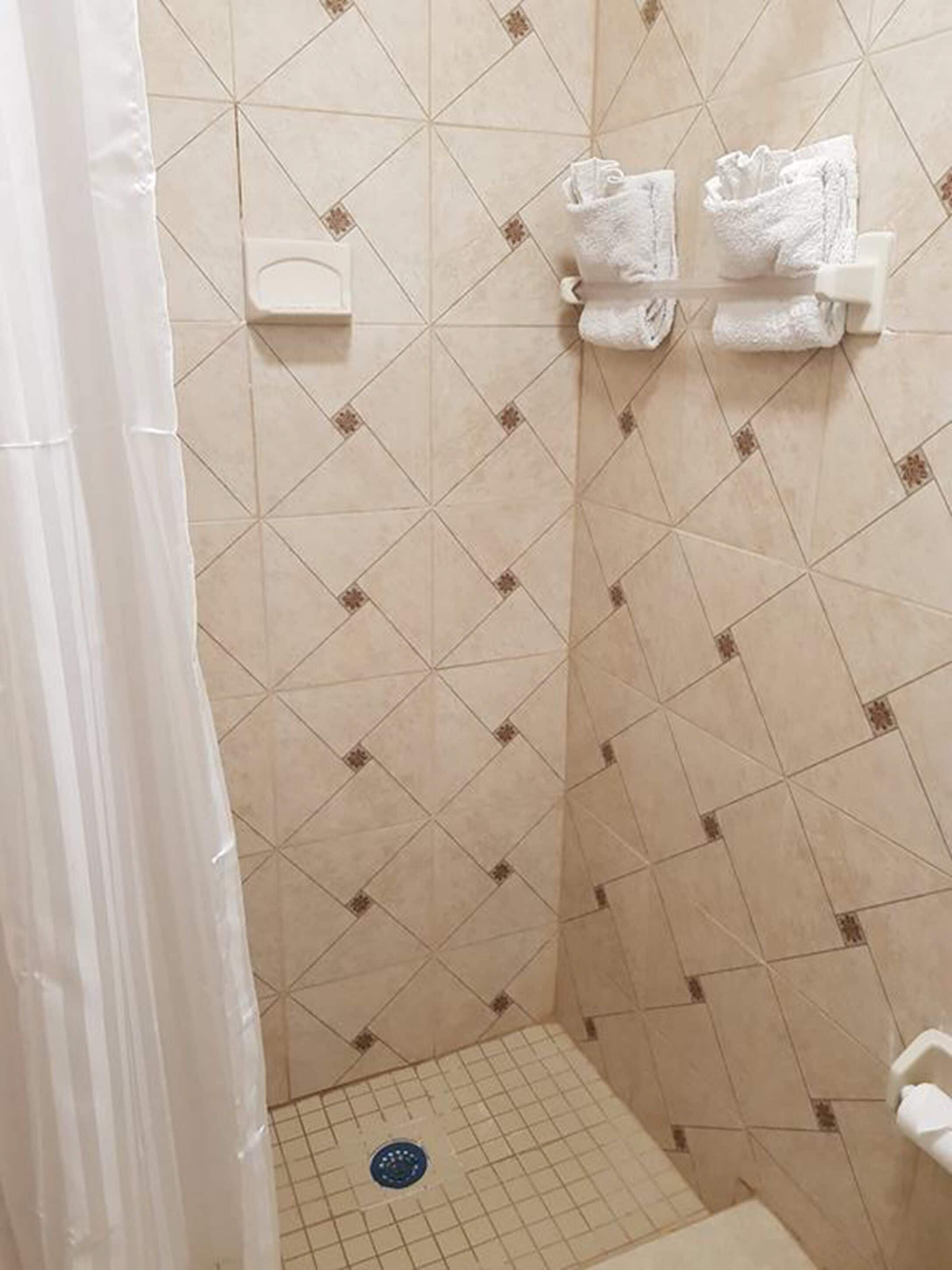 Un espacio de ducha con paredes de azulejos color beige y suelo con diseño de cuadrícula.