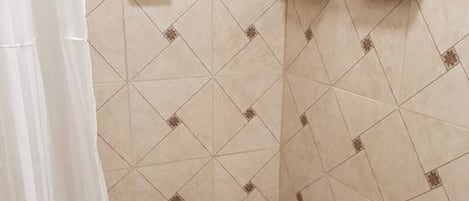 Un espacio de ducha con paredes de azulejos color beige y suelo con diseño de cuadrícula.