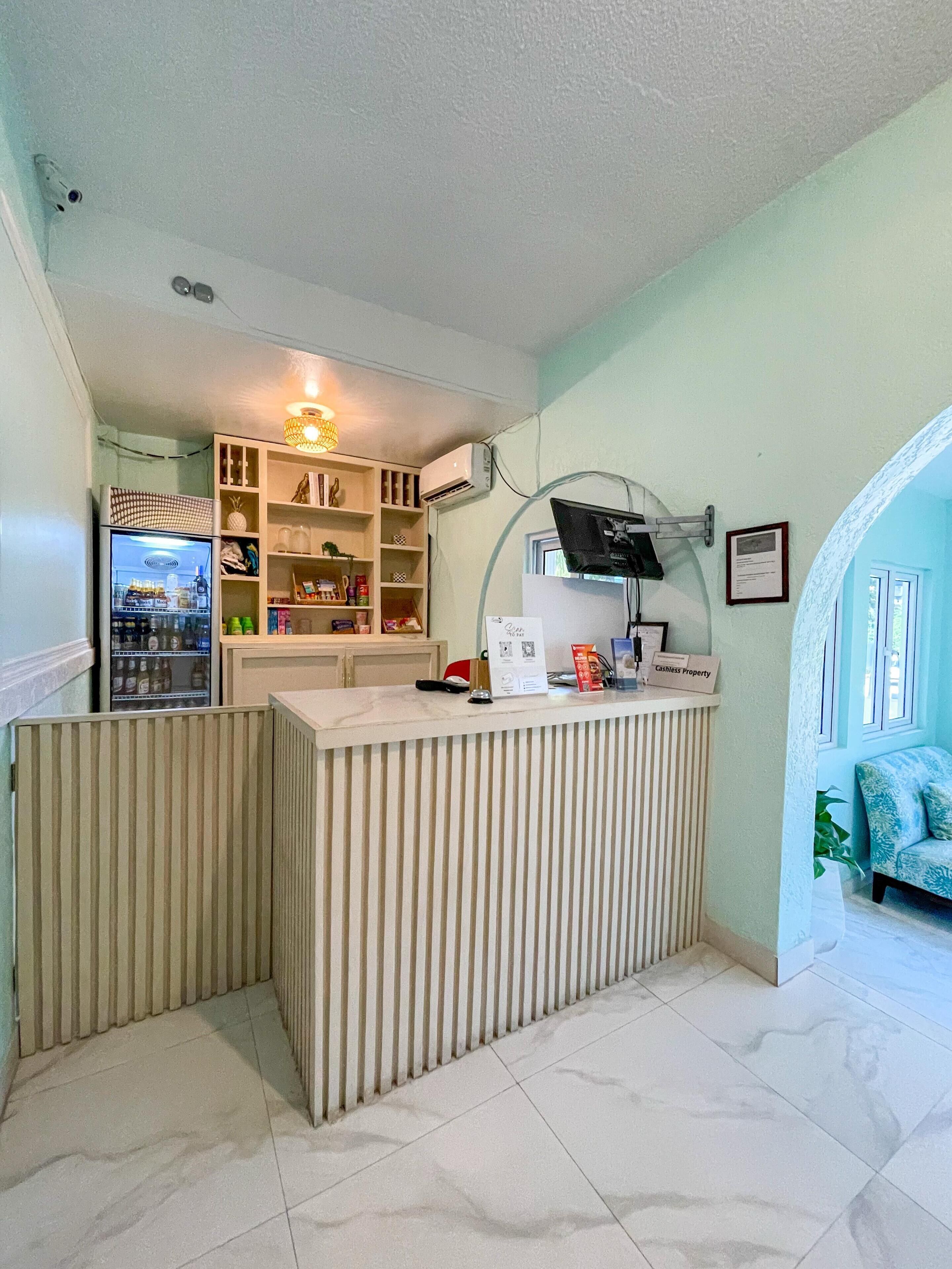 Zona de recepción con mostrador, un refrigerador lleno de bebidas, aire acondicionado de pared y lámpara en el techo.