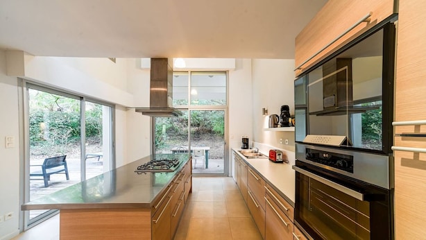 Una cocina moderna con una isla central, electrodomésticos de acero inoxidable y amplias ventanas con vistas al exterior.