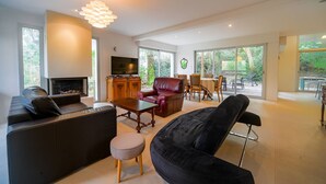 Una sala de estar amplia con chimenea, sofás de cuero, un comedor con mesa y sillas, y ventanas grandes con vistas al exterior.