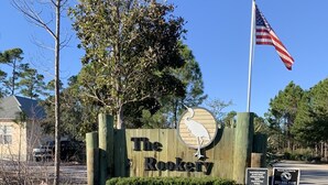 A wooden sign with "The Rookery" and a bird logo, an American flag, and a security notice. - Sandy Lane Cottage is family friendly! (Gulf Shores)