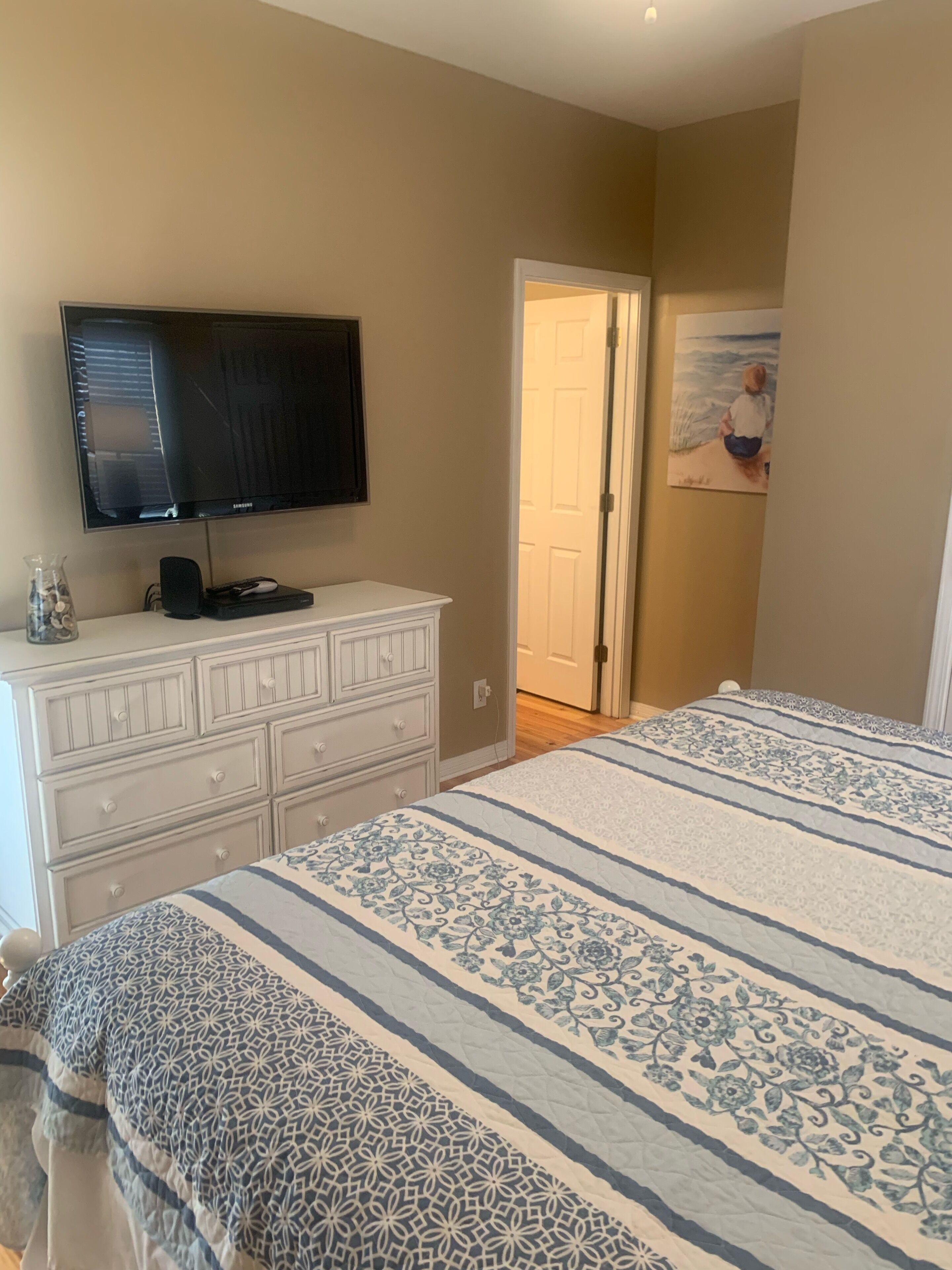 A bedroom with a bed, a dresser, a television, and a painting on the wall.