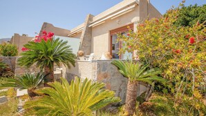 Een Mediterraanse villa met een stenen gevel, een balkon met buitenmeubilair en weelderige tropische planten.