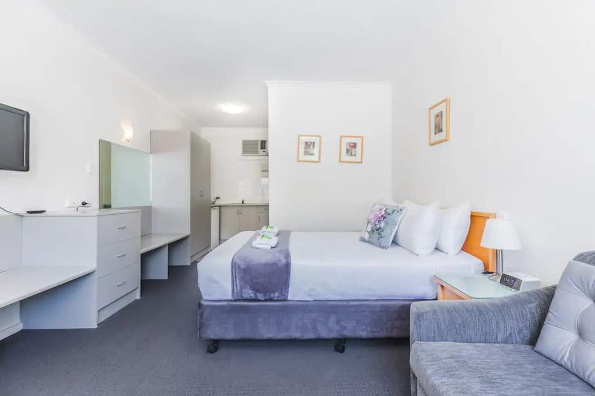 Quarto de hotel moderno com cama, escrivaninha, cadeira e mesa pequena.