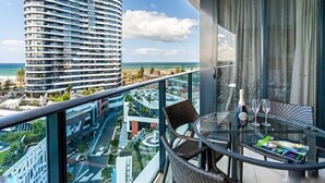 Un balcon avec une table en verre, des chaises, une bouteille de champagne et un magazine.