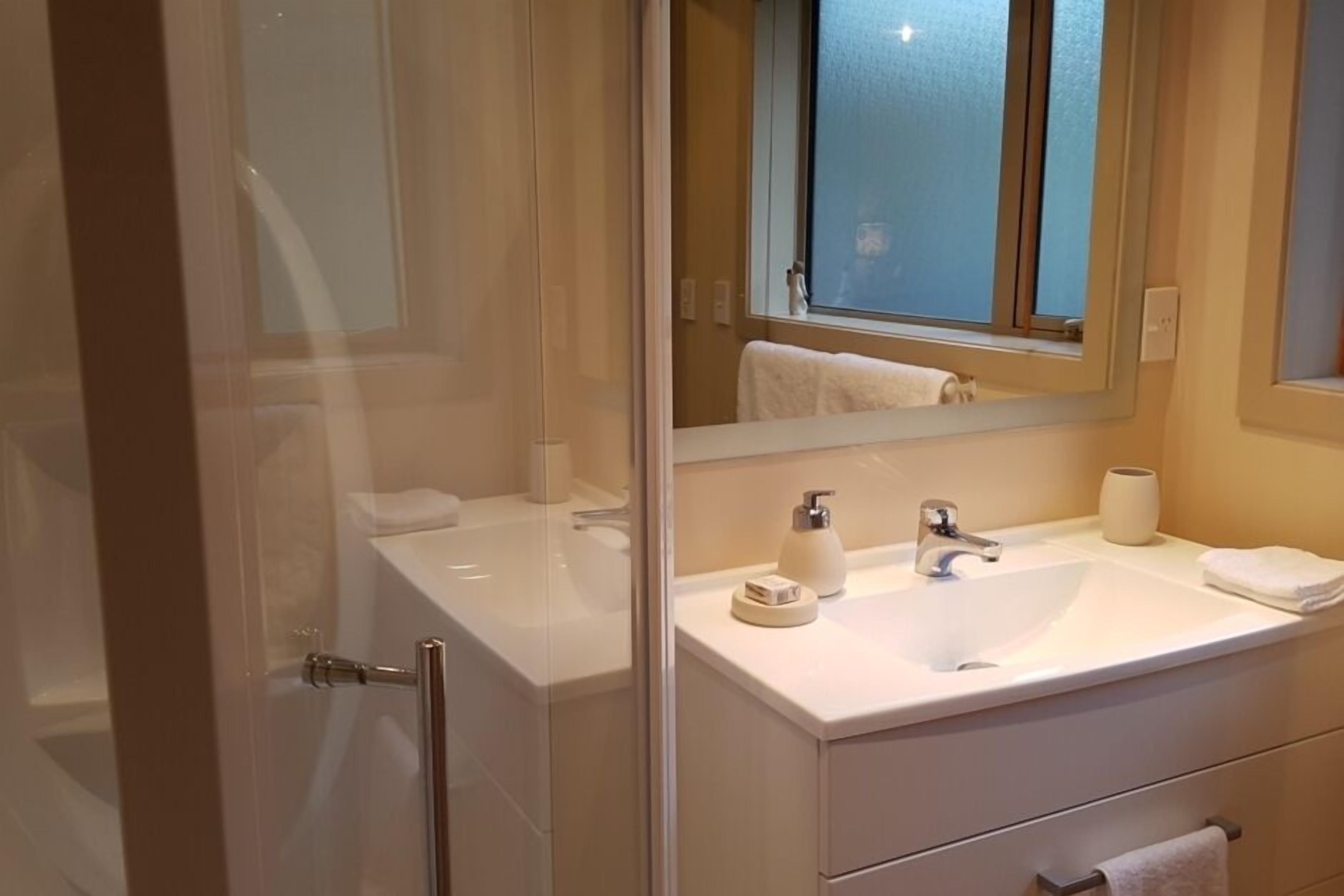 Un baño moderno con cabina de ducha de vidrio, un lavamanos blanco y un mueble de tocador con espejo.