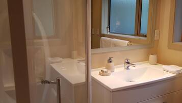 Un baño moderno con cabina de ducha de vidrio, un lavamanos blanco y un mueble de tocador con espejo.
