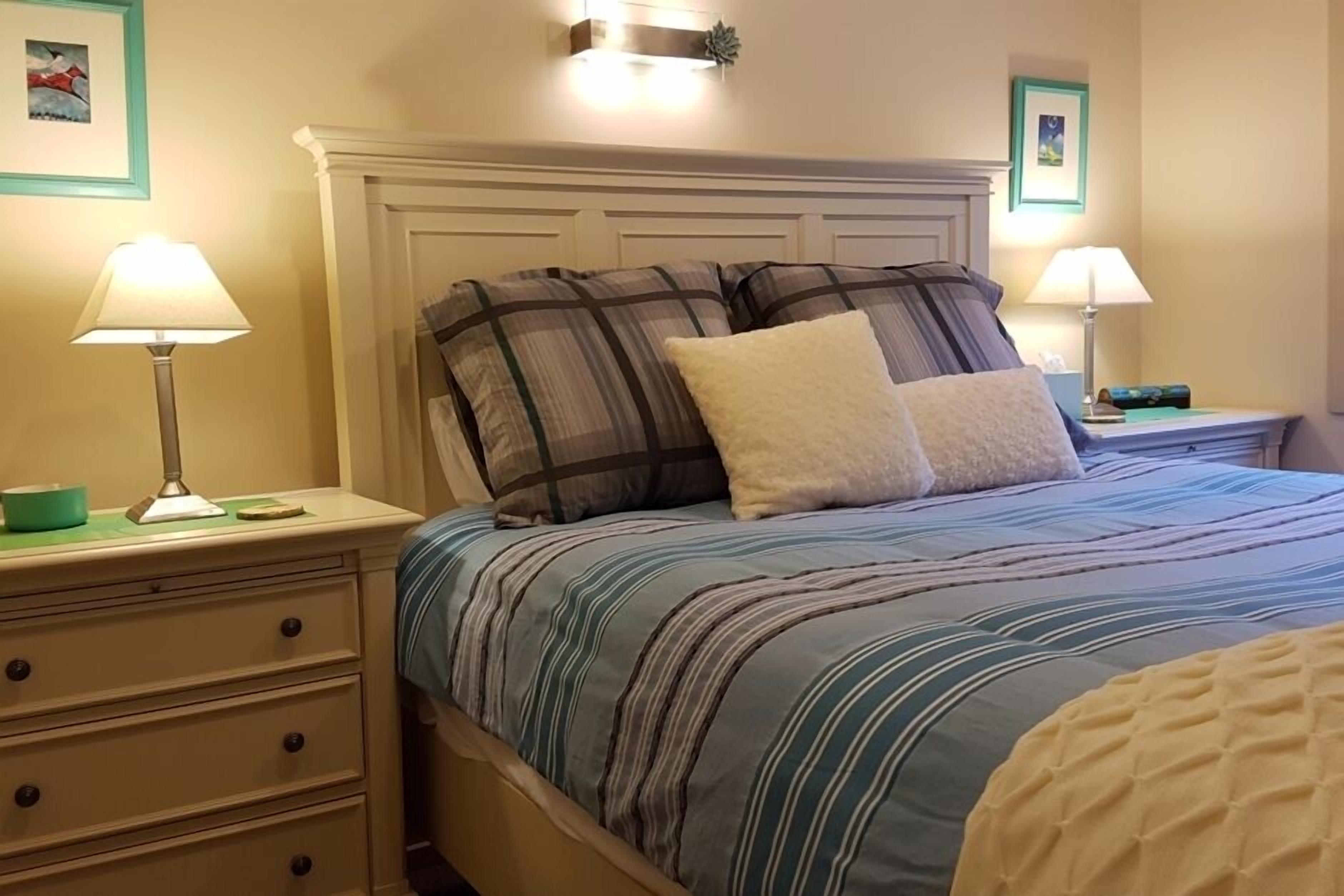 A neatly made bed with striped bedding, two bedside tables with lamps, and a dresser with drawers.