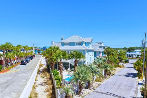 Une propriété située en bord de mer, comprenant une grande maison, une piscine et une rue bordée de palmiers.