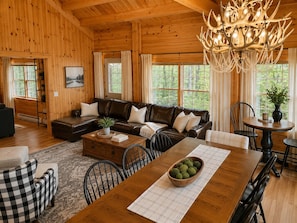 A wooden interior with a sofa, dining table, chairs, and a chandelier.