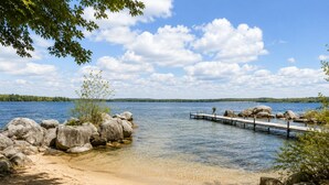 Une scène au bord d’un lac, avec une jetée en bois qui s’avance dans l’eau, entourée de gros rochers et d’arbres.