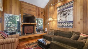 Una habitación con paneles de madera, una chimenea, un sofá, una televisión y un cartel con un lobo gris.