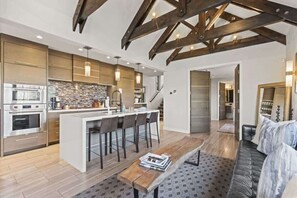 Una cocina moderna con una isla central, taburetes de bar y una zona de comedor con sofá y mesa de centro.