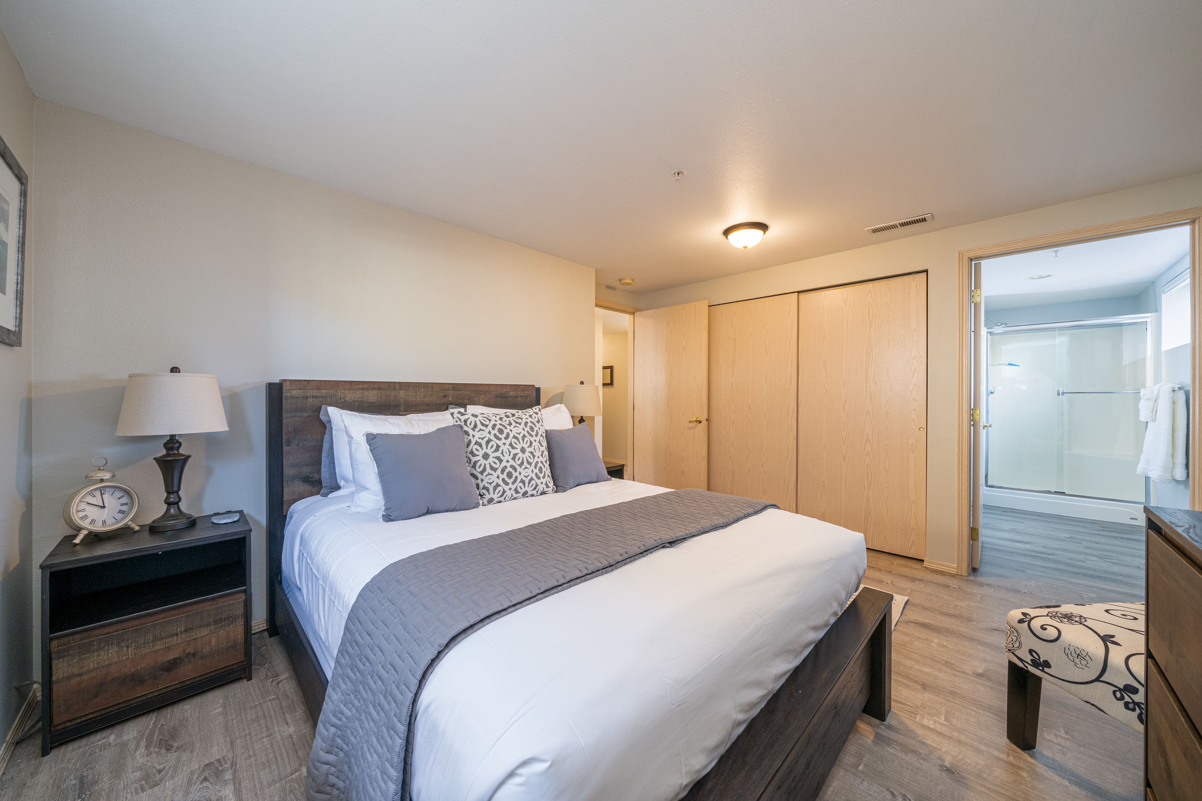 A bedroom with a bed, bedside table, lamp, and a view of a bathroom.