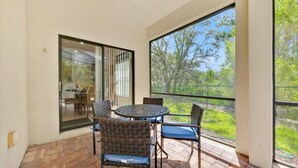A patio with a round table and chairs, large windows with a view of greenery, and a door leading to an indoor area. - More 4 your Money w/ Private South Facing Pool (Kissimmee)