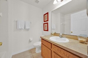 A bathroom with a white toilet, a sink, and a mirror. There are two framed pictures on the wall. - More 4 your Money w/ Private South Facing Pool (Kissimmee)