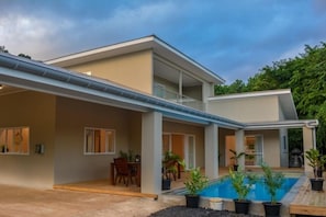 Uma casa moderna de dois andares com varanda coberta, piscina e área de refeições.