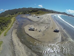 Luchtbeeld van een strand met een onverharde pad, voertuigen en mensen.