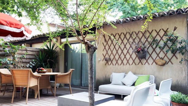 Eine Terrasse mit Korbmöbeln, einem weißen Sofa und einem kleinen Baum.