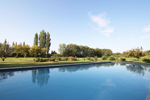 Una piscina con superficie riflettente, circondata da un prato curato e alberi.