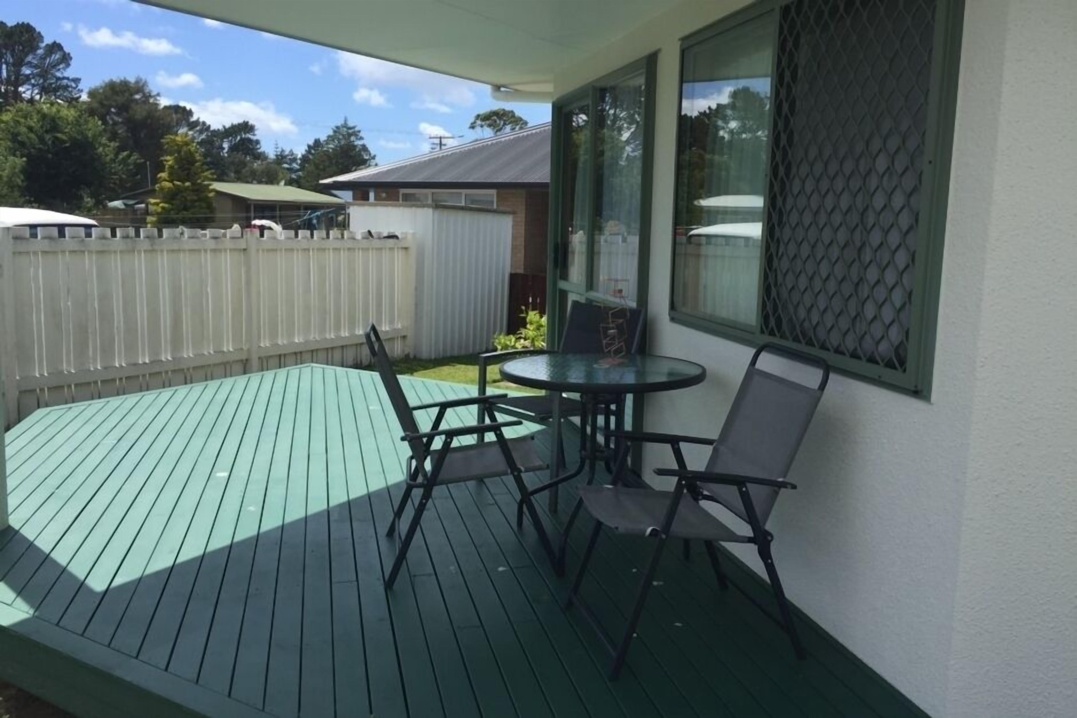 A covered outdoor patio with a green deck, a round table, and four chairs.