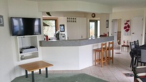 Un salon moderne avec un téléviseur, une petite table en bois, un tapis moelleux et un coin cuisine doté d’un comptoir-bar et de chaises.