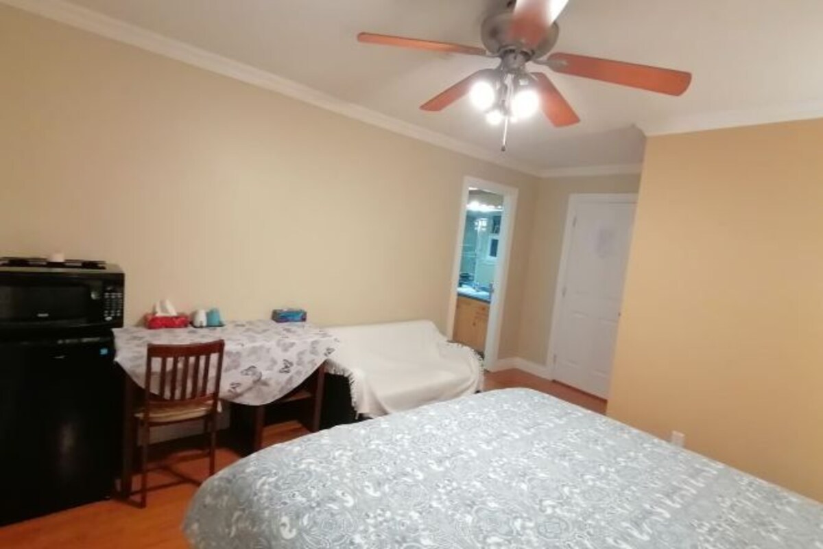 A bedroom with a bed, a ceiling fan, a dining area with a table and chairs, and a microwave.