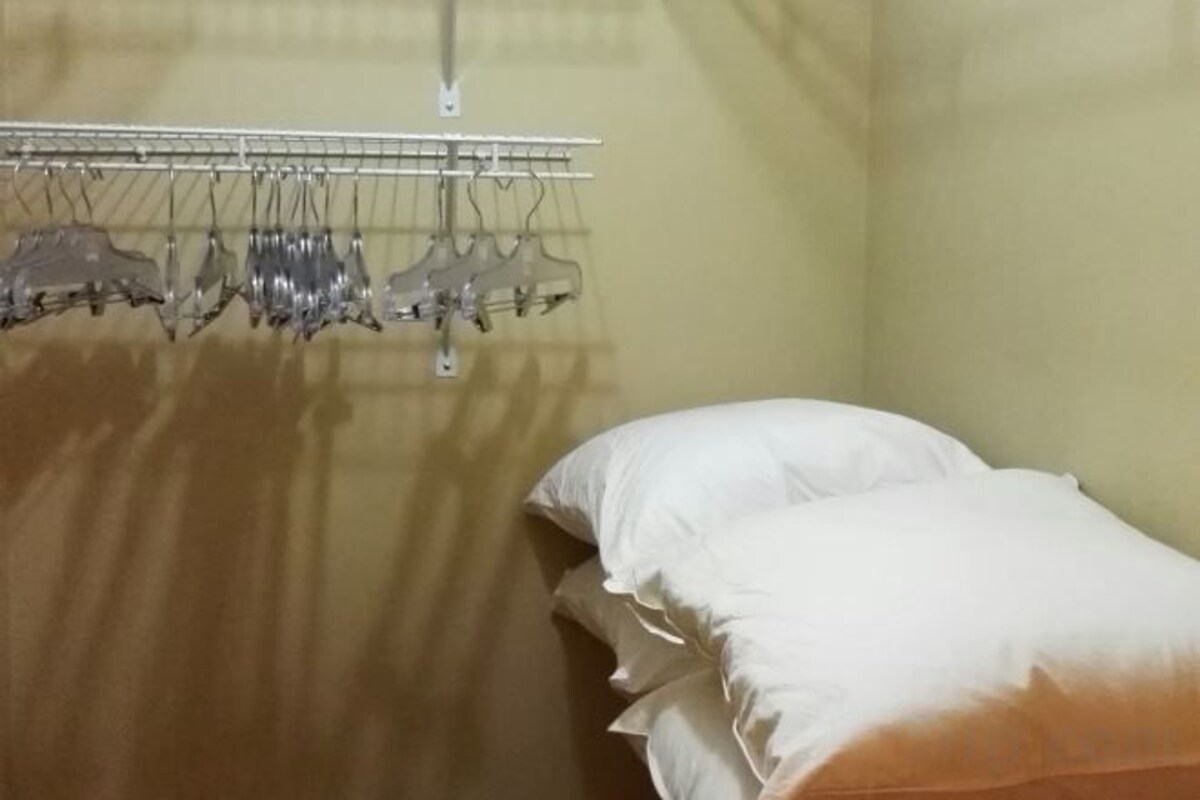 A room with a bed, a hanging clothes rack, and a wall-mounted light fixture.