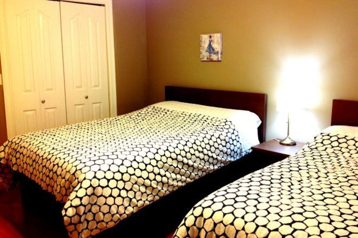 A hotel room with two beds, a nightstand, a lamp, and a painting on the wall.