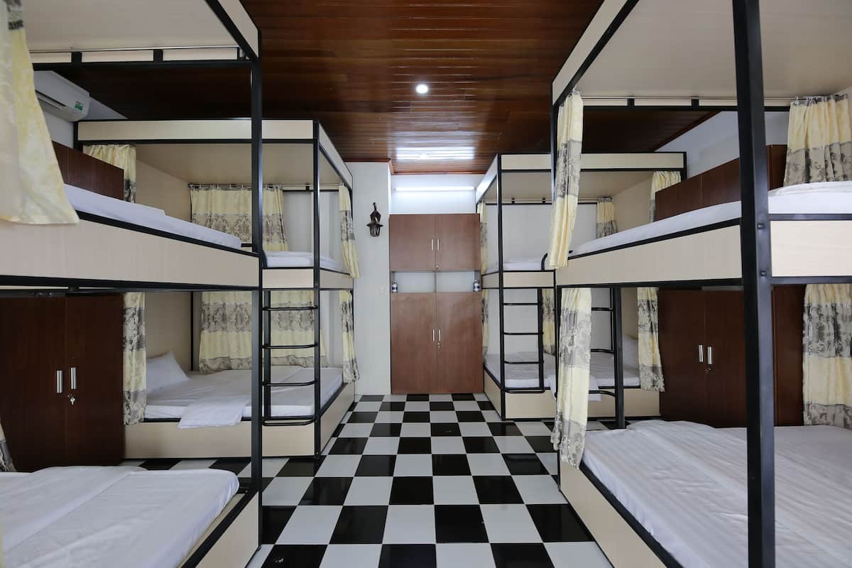 Une chambre de dortoir avec des lits superposés, un sol à carreaux, un plafond en bois et une armoire.