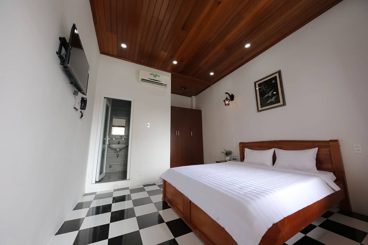 Une chambre avec un sol à carreaux, un plafond en bois, un lit avec une literie blanche, une armoire et un tableau encadré au mur.