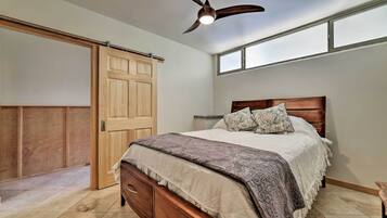 Quarto com cama, cabeceira de madeira, ventilador de teto, janela e porta deslizante.