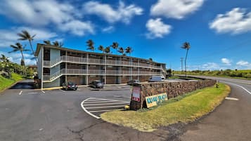 A multi-story motel with a parking lot, palm trees, and a clear sky.