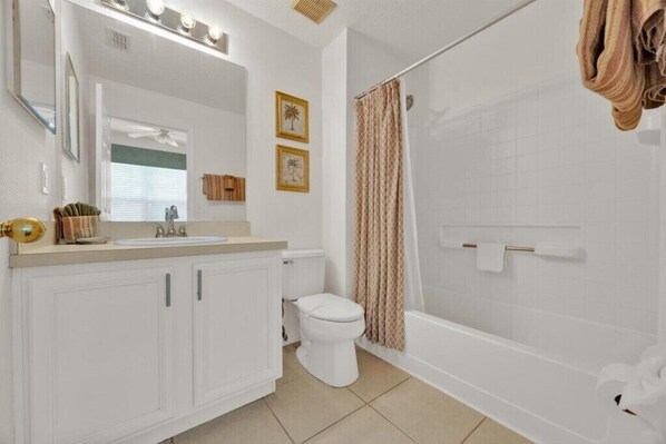 Une salle de bain moderne avec un lavabo, des toilettes et une baignoire, tous de couleur blanche. Des tableaux encadrés ornent le mur, et un porte-serviettes est également présent.