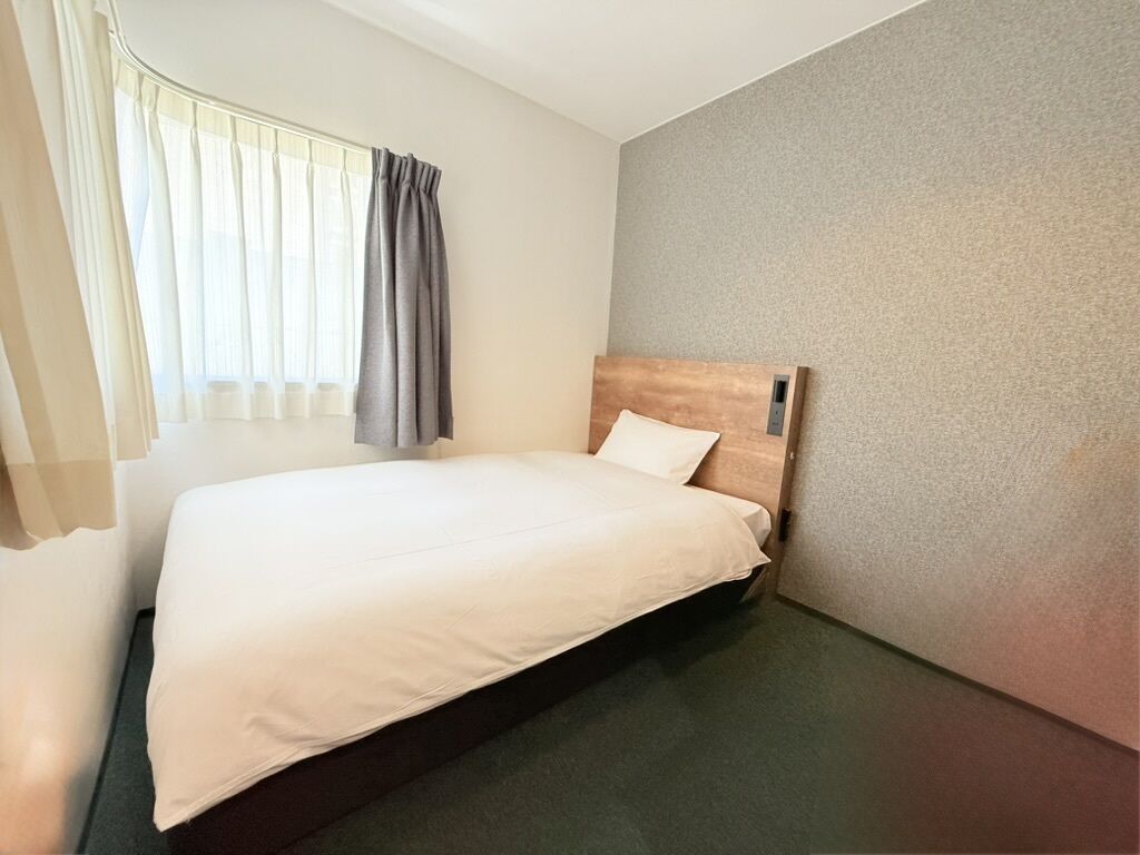 A hotel room with a bed, a window with curtains, and a textured wall.