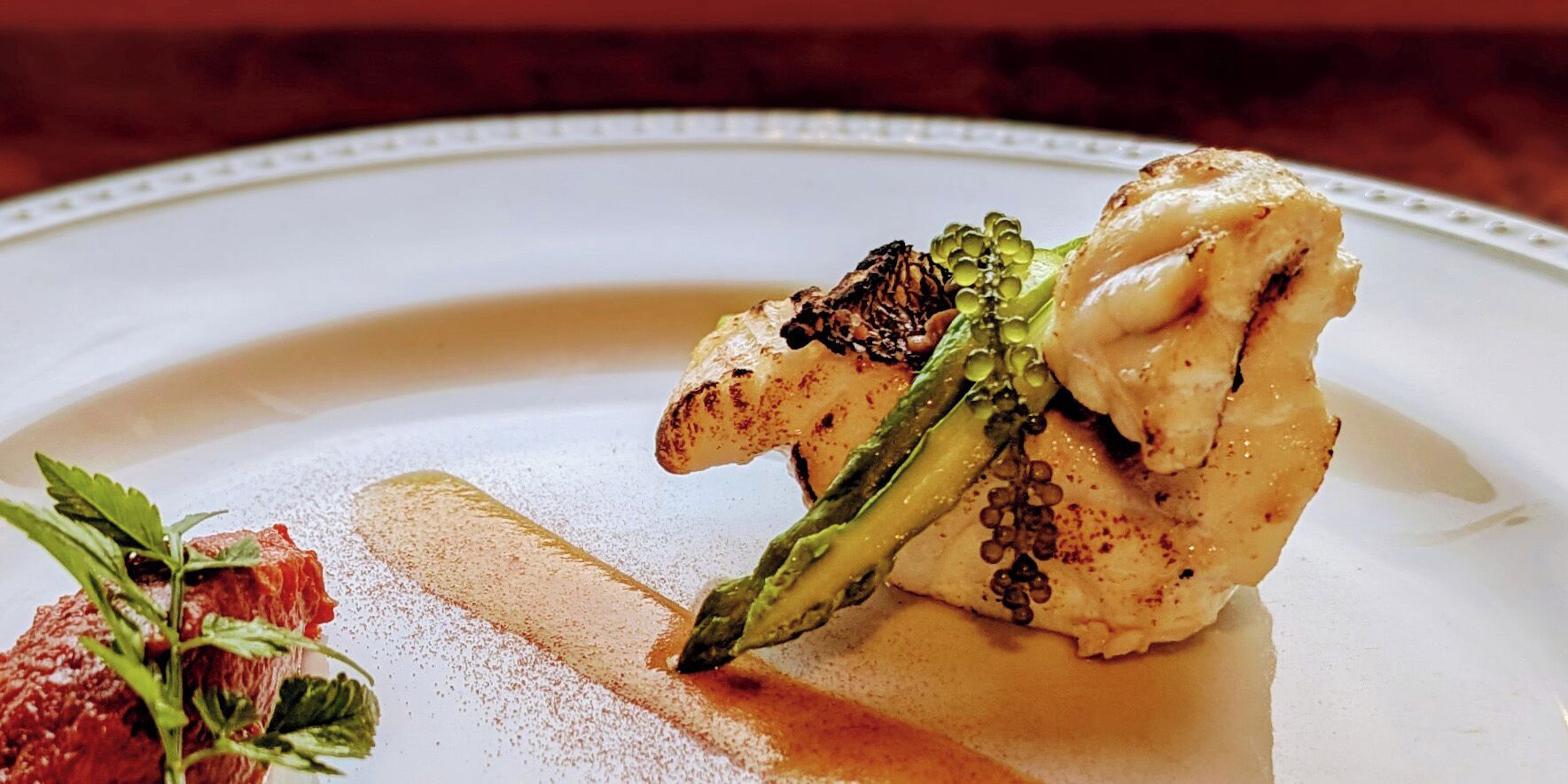 A white plate with a piece of grilled chicken, asparagus, and a small garnish.