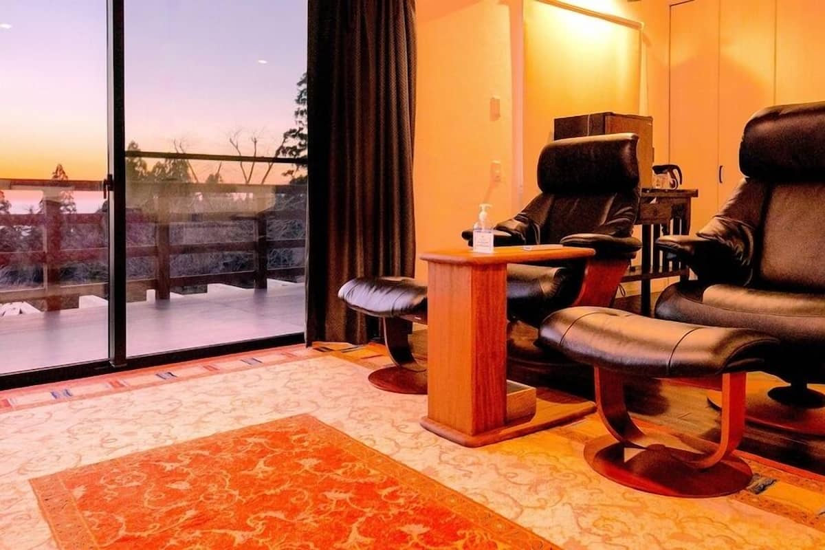 Una habitación con dos sillones de cuero, una mesita de madera y un ventanal con vistas a árboles y un edificio.