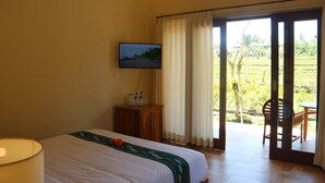 A hotel room with a bed, a television, a wooden cabinet, and a view of a garden through a sliding door. - Senja D'Ubud (Ubud)