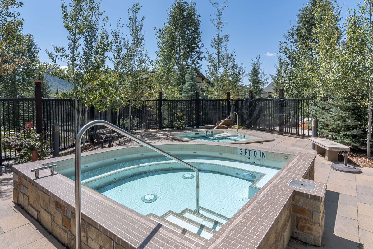 Une piscine intérieure de 90 cm de profondeur, avec un bord carrelé, entourée d’une clôture noire et d’arbres.