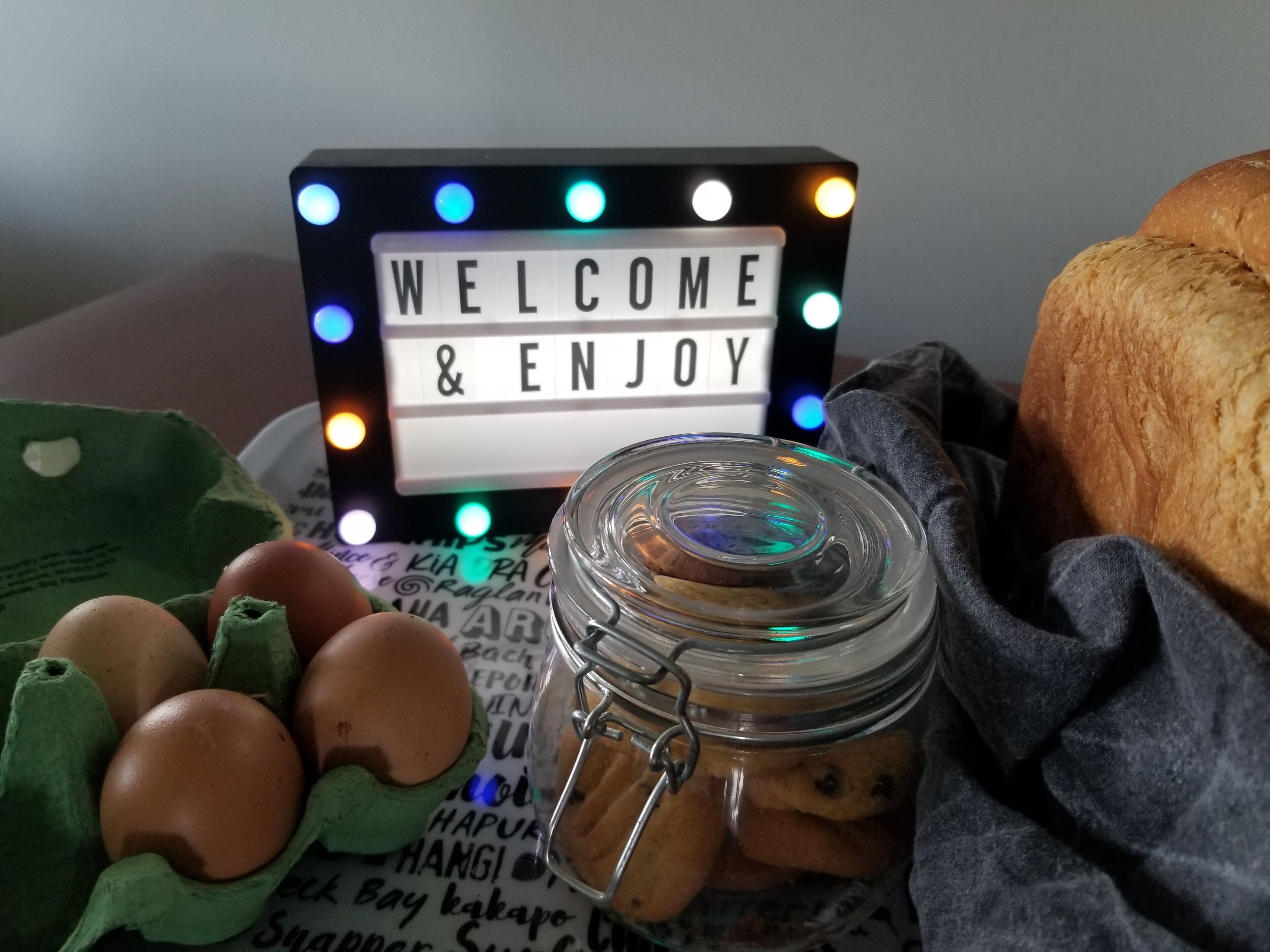 Un letrero de bienvenida con luces, un tarro de galletas, huevos y una hogaza de pan.