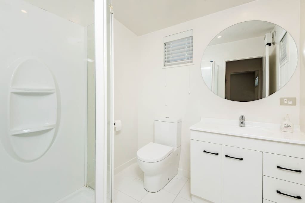 A modern bathroom with a glass shower enclosure, a toilet, a sink with a mirror, and white cabinetry.