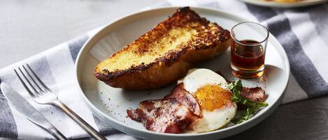 A plate with toast, bacon, and a fried egg, accompanied by a small glass of tea.